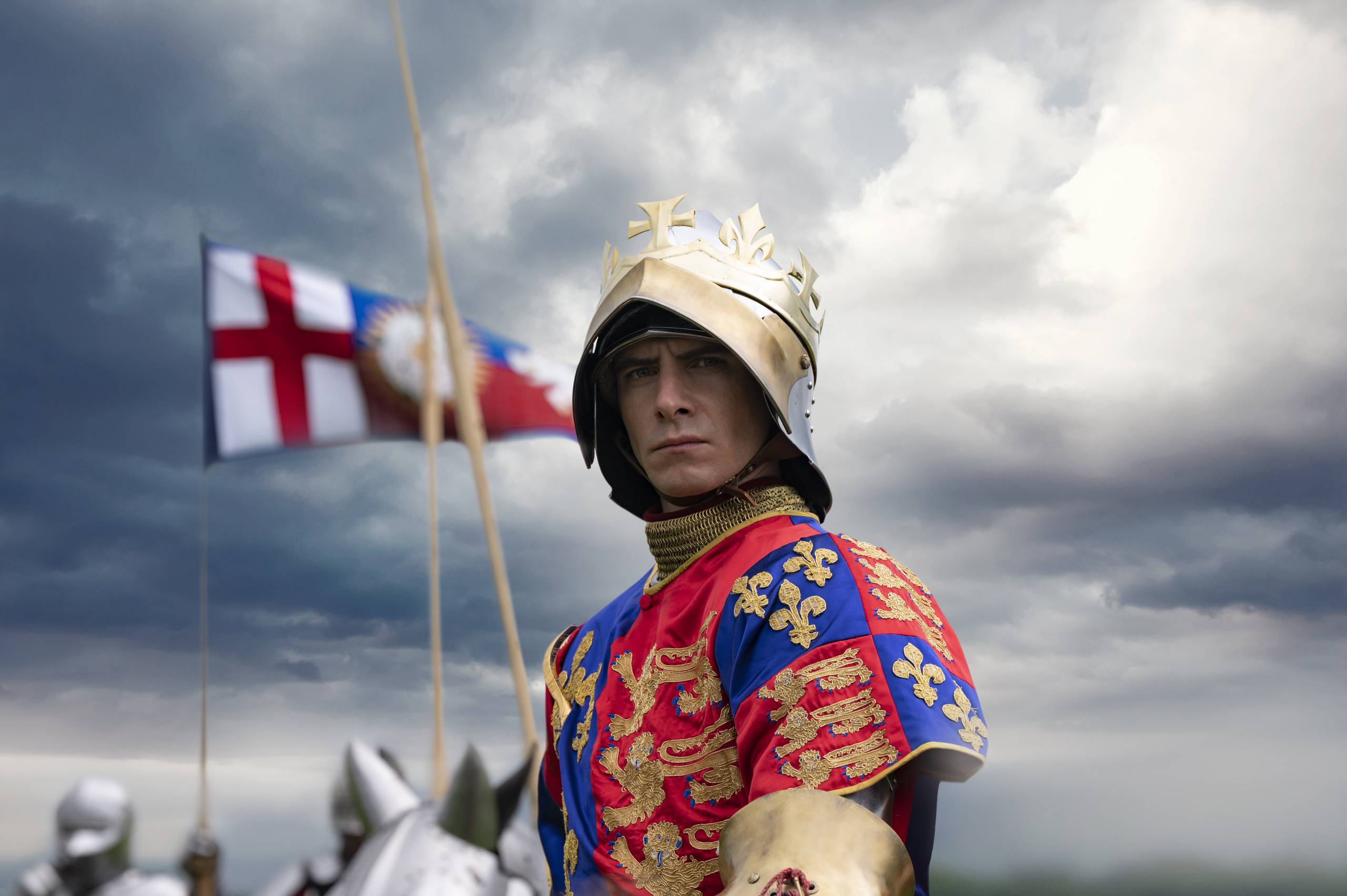 A white man in a helmet and red and blue regalia sits on an armored horse