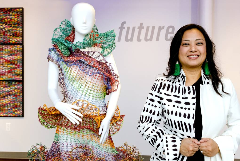 A smiling Asian woman stands next to a mannequin in a netting dress
