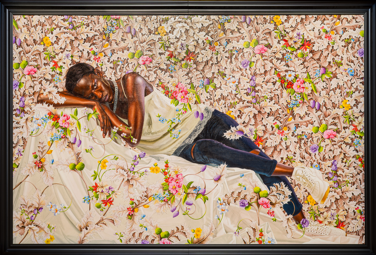A Black woman leans on a white draped surface surrounded by white blossoms