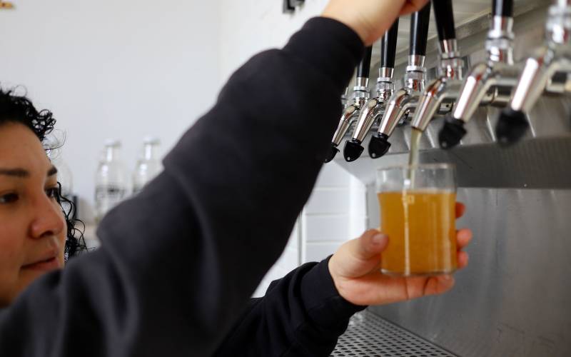 a kombucha maker pours a fresh glass from the brewer's tap