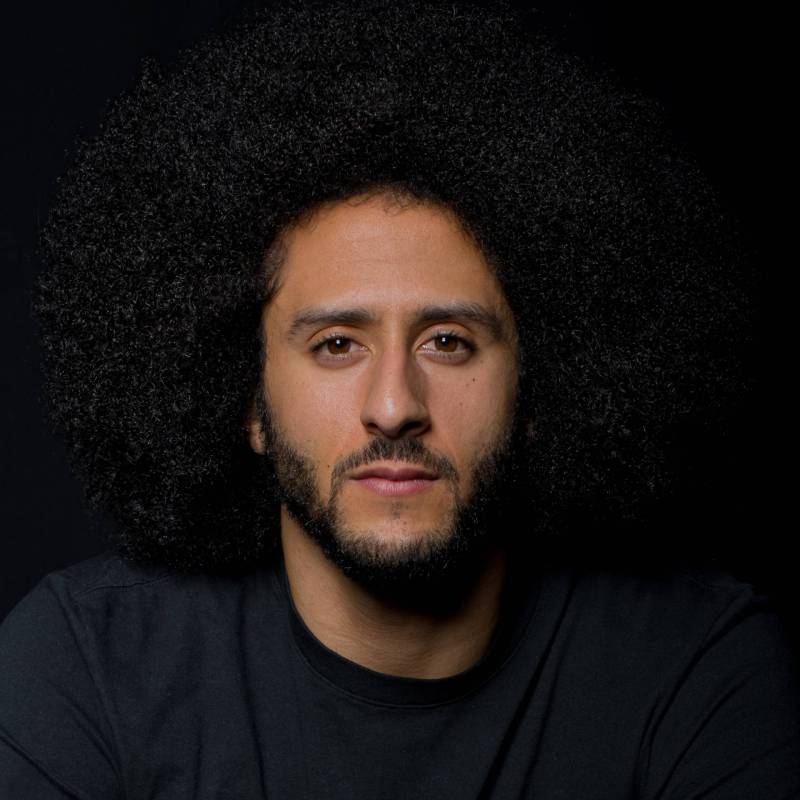 A mixed race man with close-cropped beard and large afro faces the camera.