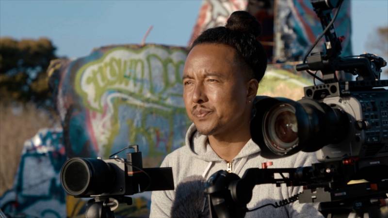 Filmmaker Adamu Chan stares into the distance while holding his camera.
