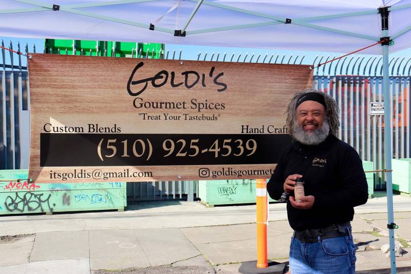 A man stands in front of his spice booth at the market