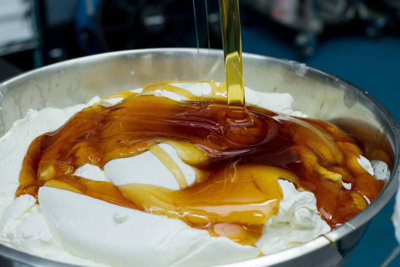 A metal bowl full of yoghurt getting drizzled with a generous helping of honey.