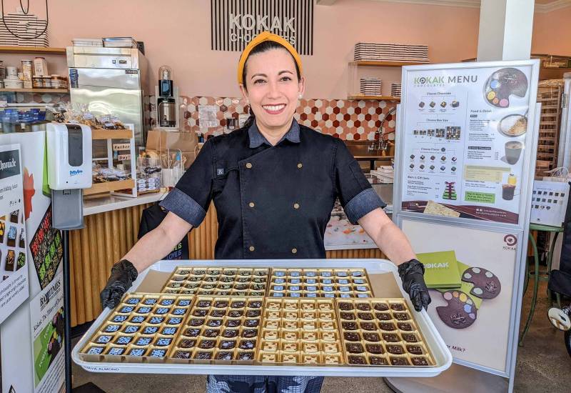 the Filipina chocolatier, Carol Gancia, stands inside her chocolate shop in San Francisco, holding a large tray of artfully decorated chocolates