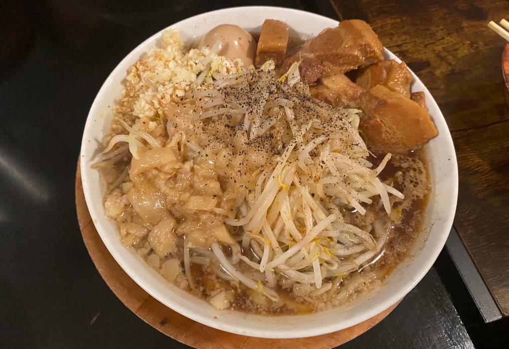 Bowl of ramen with an exorbitant amount of toppings: bean sprouts, chopped raw garlic, pork belly, pork fat and marinated egg.