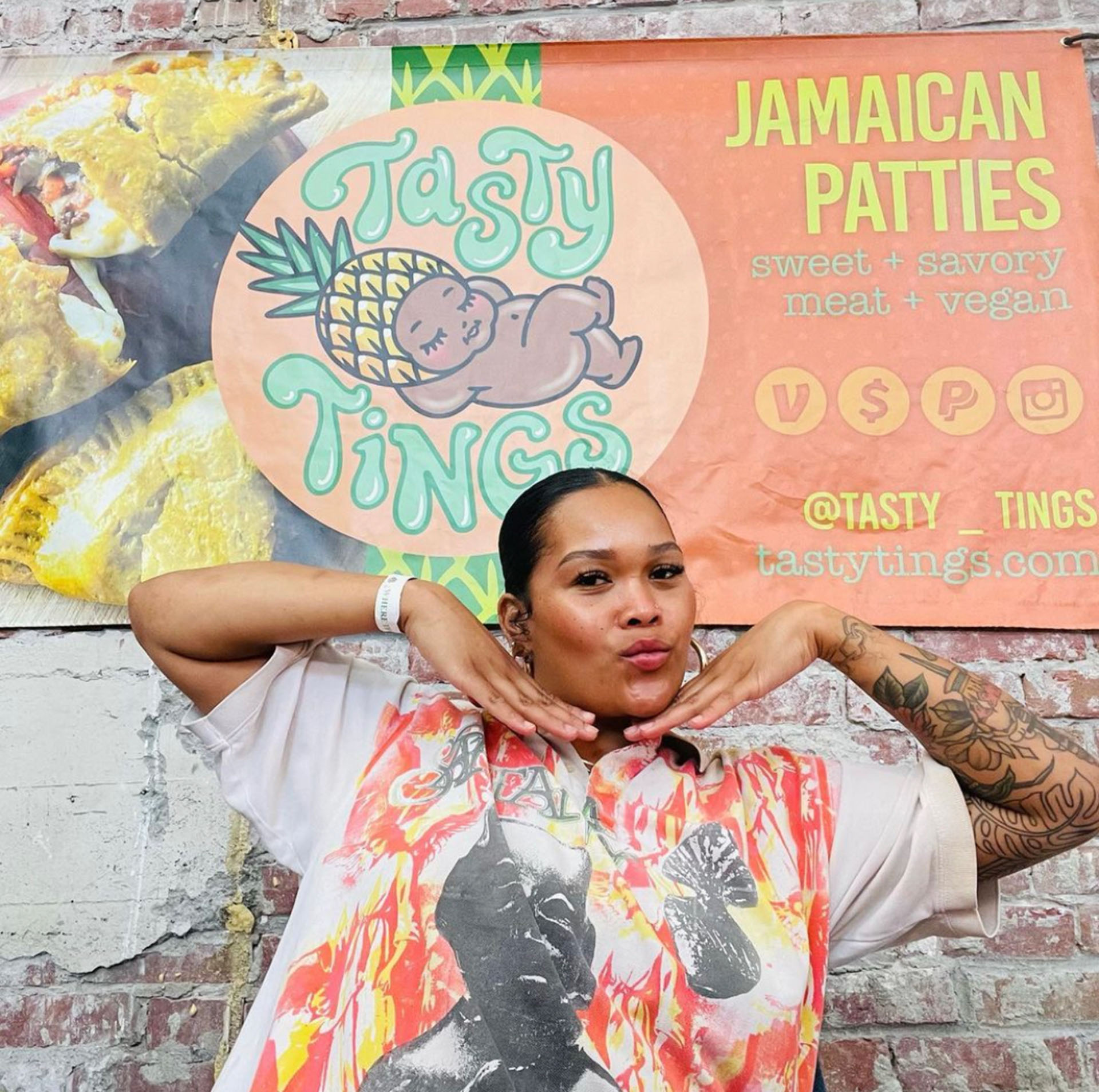 The owner of Tasty Tings poses in front of a sign for her Jamaican food pop up.