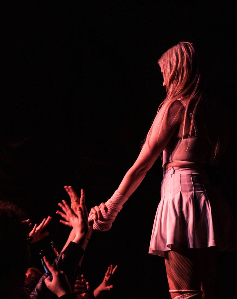 A young woman with blonde hair is seen from the side ona stage holding a fan's hand
