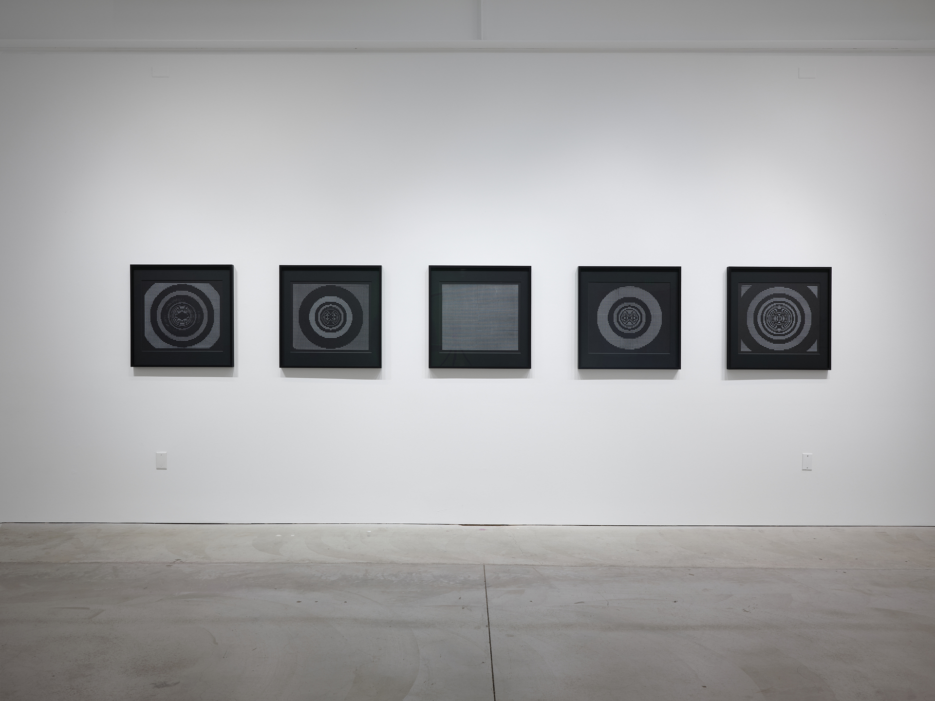 Five framed prints on white wall, each square with circles of white text on black paper