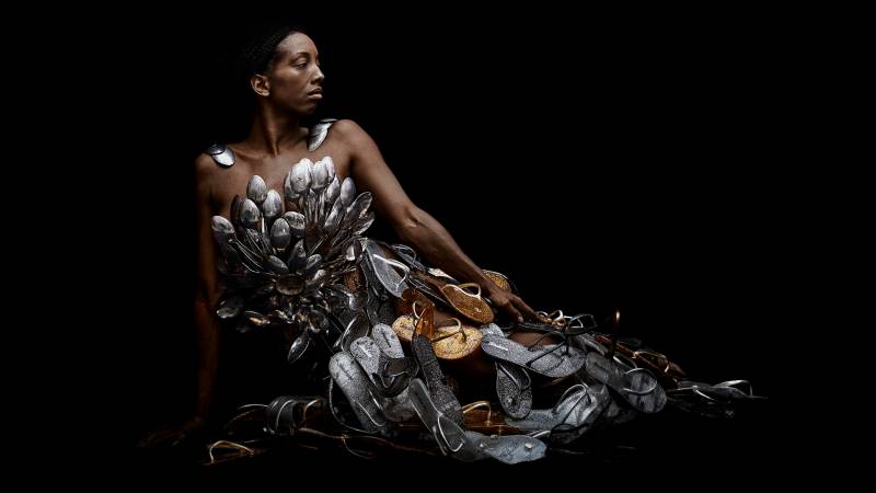 Photograph of reclining Black woman looking to right adorned with silver spoons and gold and silver shoes