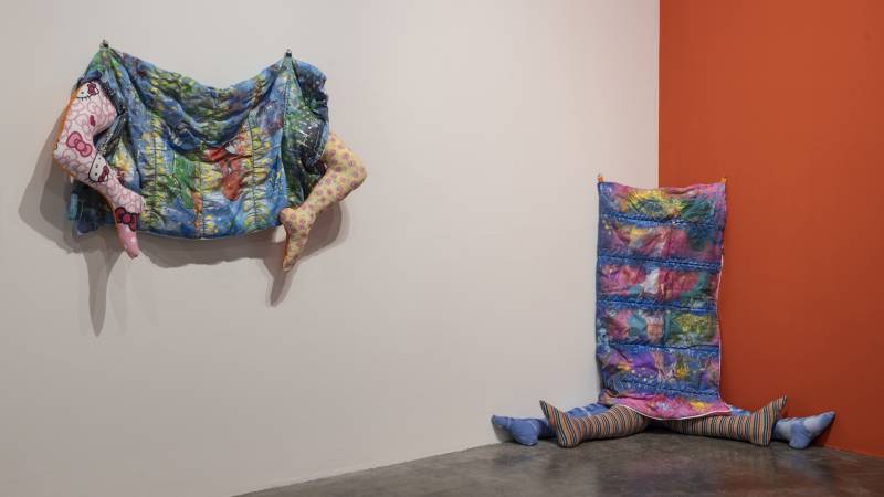 Two textile pieces with legs: one mounted to wall as if jumping up, another slumped in corner
