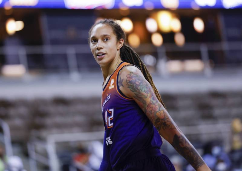 A woman with long dreadlocks tied back half-smiles as she strides across a basketball court.