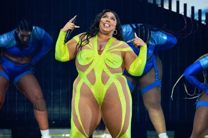 A plus-size Black woman performs onstage wearing a sheer bodysuit with neon yellow details.