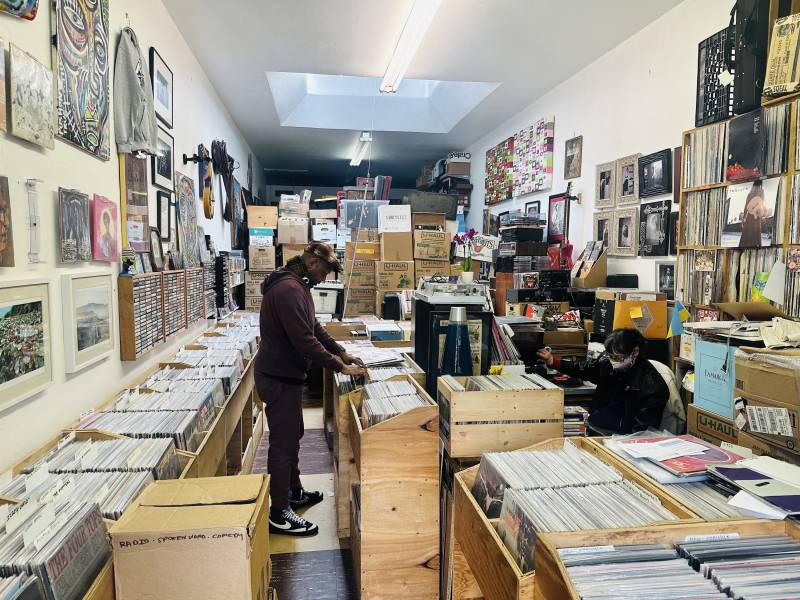 a man looks through vinyl records in a record store while an employee sits behind the desk