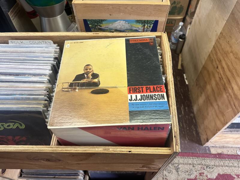 a bin of records with a record by jazz artist J.J. Johnson called 'First Place' on top