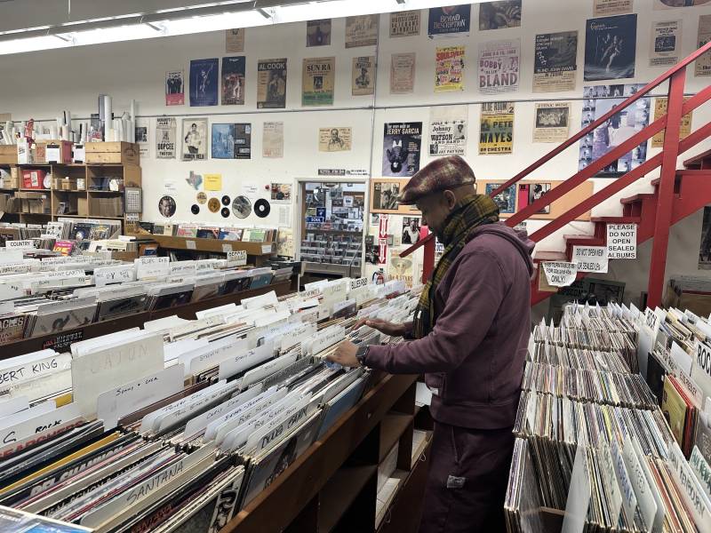 a man in a purple hoodie flips through records in a record store