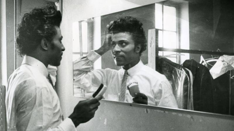 Black-and-white photograph of young Black man combing his pompadour in mirror
