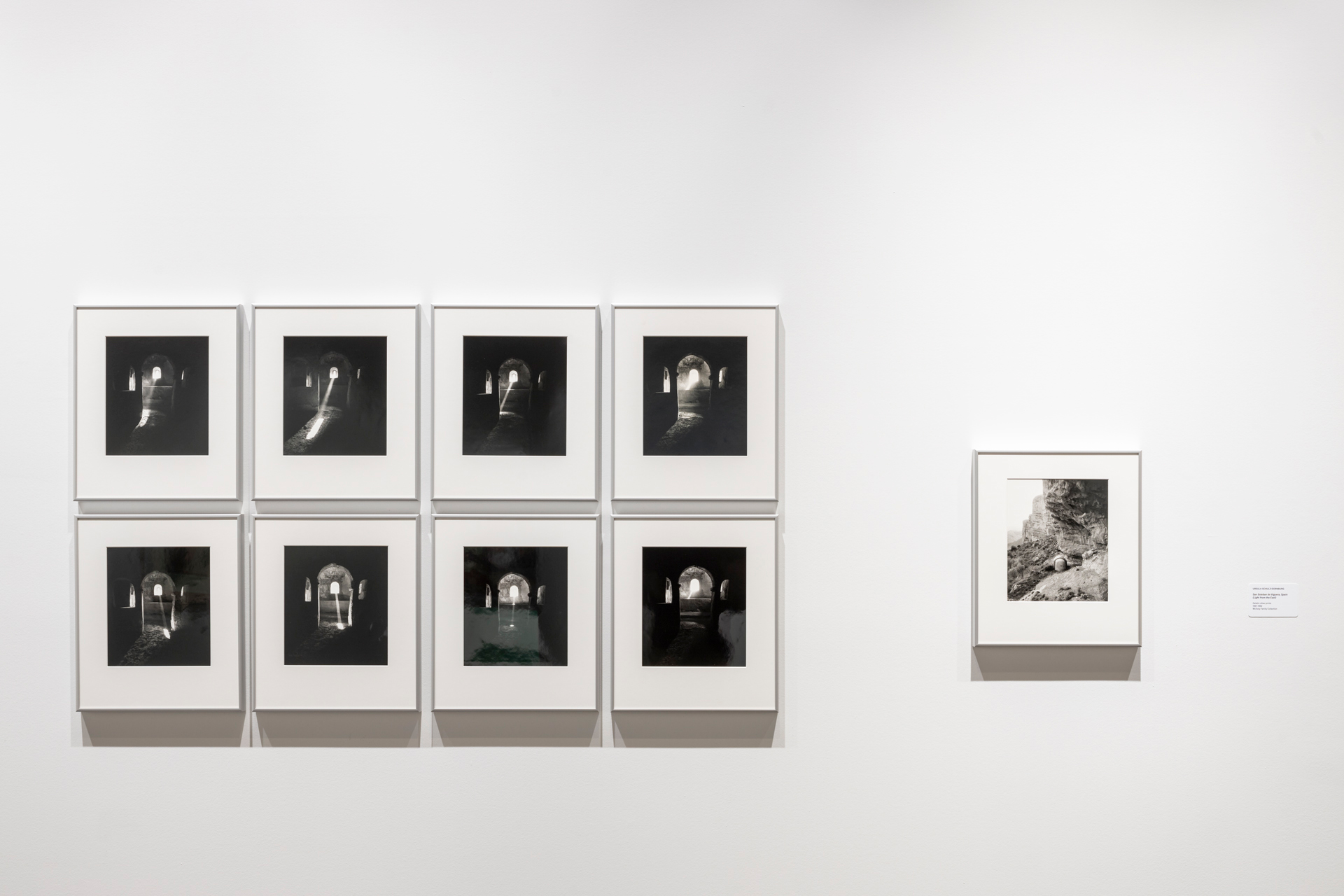 Eight framed black-and-white photographs of an arched interior space hung in grid with one photograph to right