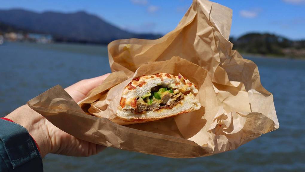 a sandwich from Davey Jones Deli is held up with Sausalito's harbor in the backround