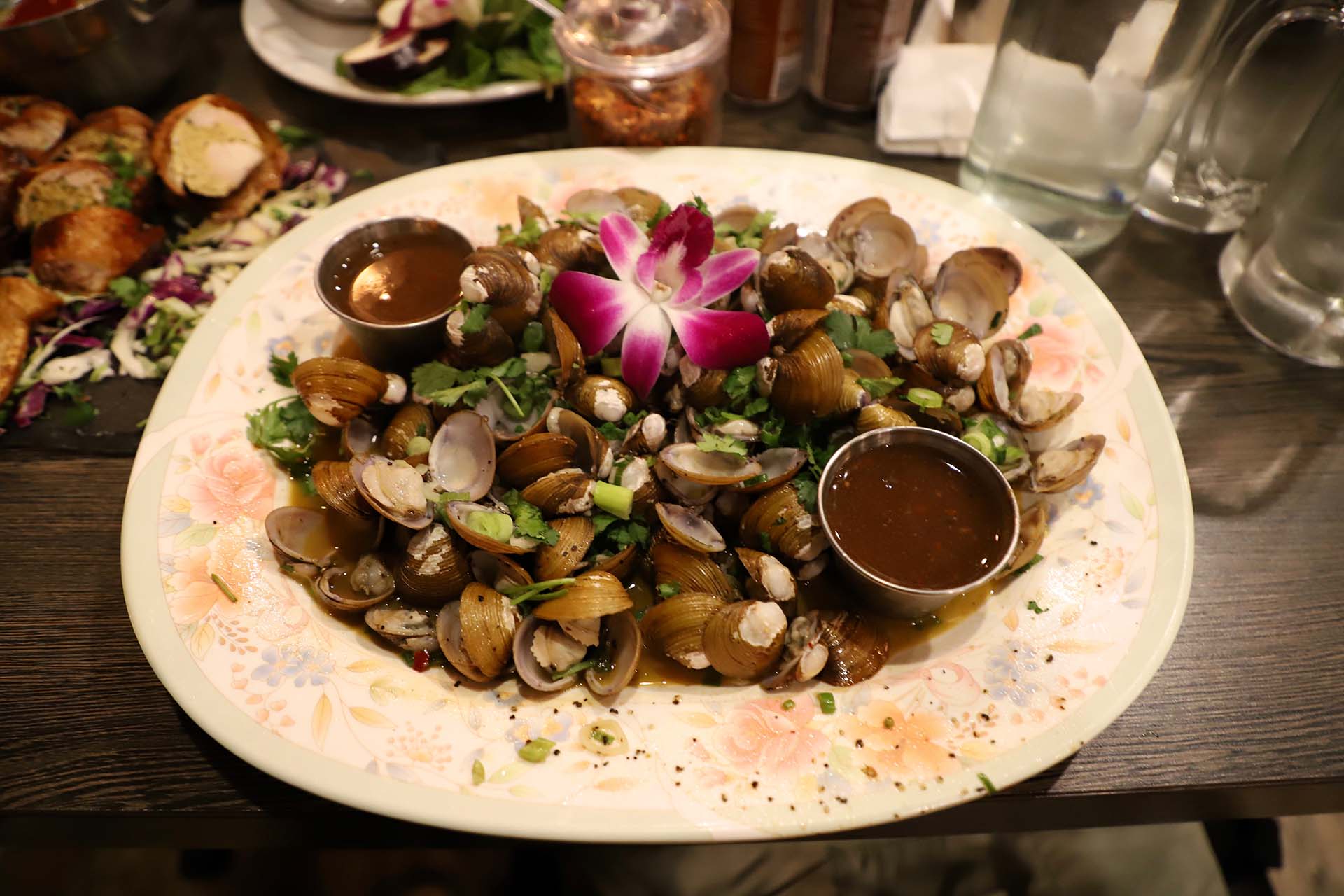 A plate of small freshwater clams topped with a decorative purple orchid blossom.
