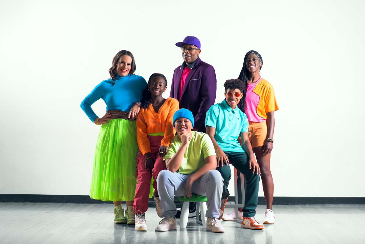 Three adults and three teens in brightly colored clothes pose and smile at camera