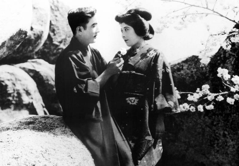 A Japanese man and woman get close near a granite boulder.