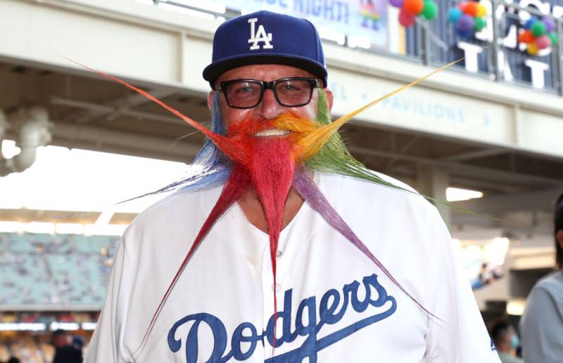 A man with a spiked, rainbow beard wears Dodgers gear. 