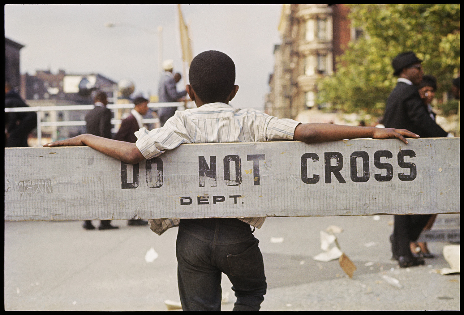 Color photograph of back of Black boy leaning against a barricade that reads 