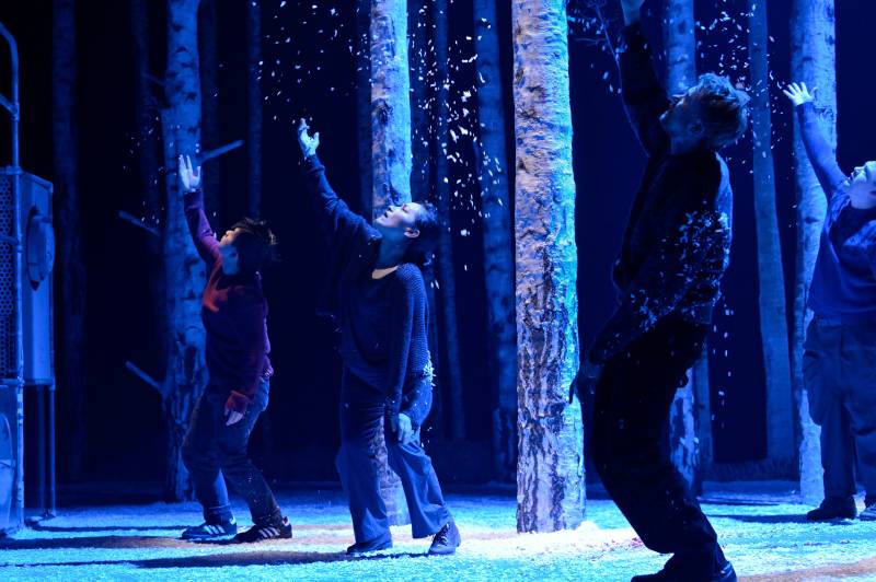 four people in blue light with fake snowfall on a stage in a play