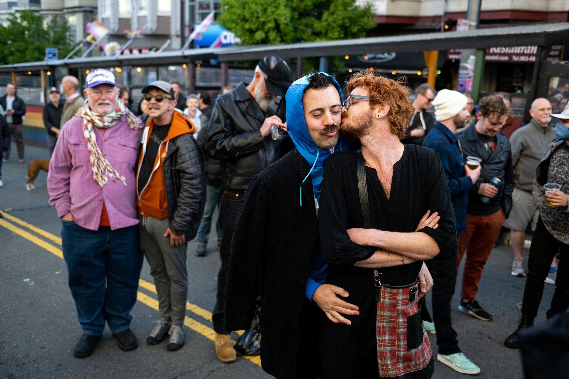 A large crowd stands on Castro Street in front of Castro Theater, and in the middle of the crowed, a young couple hugs and kisses.