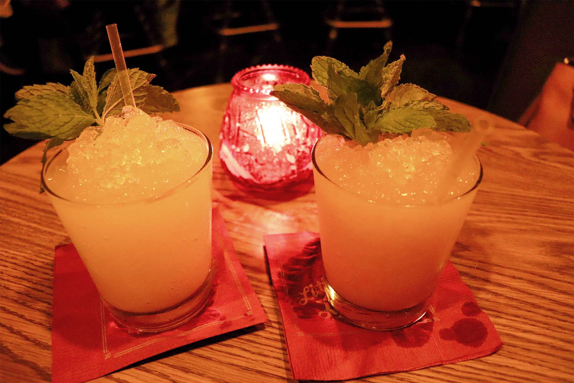 Two mint-garnished tropical cocktails, lit from behind by candle light.