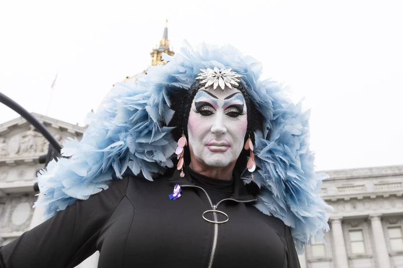 A drag queen nun wears a feather boa and white makeup.