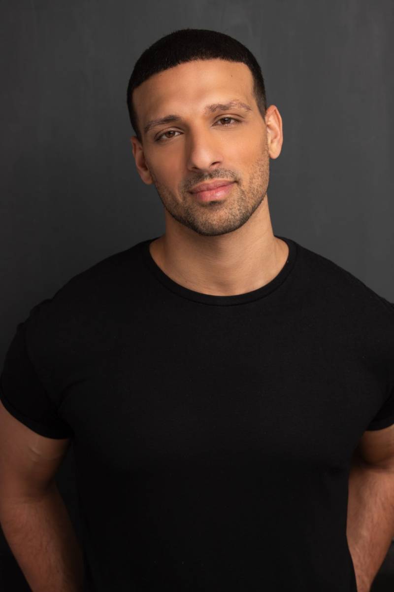 a portrait of a man with light brown skin and a very short beard wearing a black t-shirt