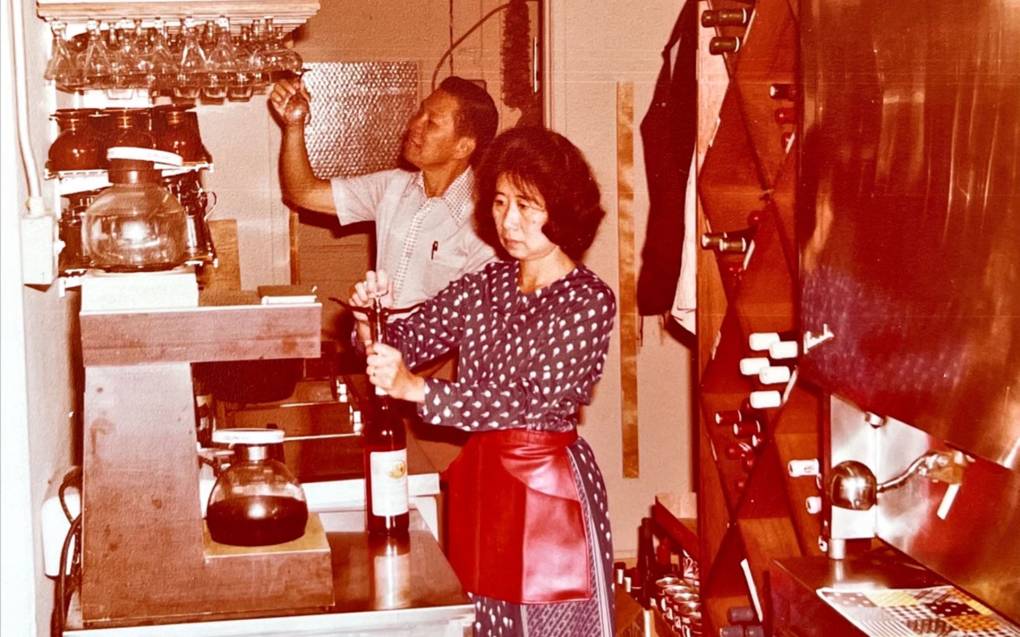 A woman in a red apron opens a bottle of wine at a restaurant in this old photograph from the 1980s.