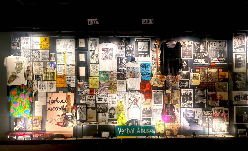 A glass case containing a densely packed array of posters, merchandise, clothing and instruments.