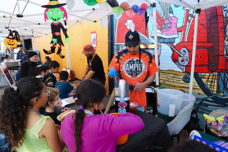 A foodmaker serves cold slushies to a group of young children at an outdoor cultural event in San Francisco