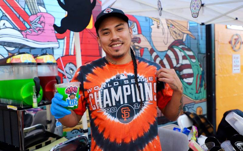 a foodmaker from San Francisco wears a Giants t-shirt and holds up a cup of his speciality beverage, Hyphy Iceez