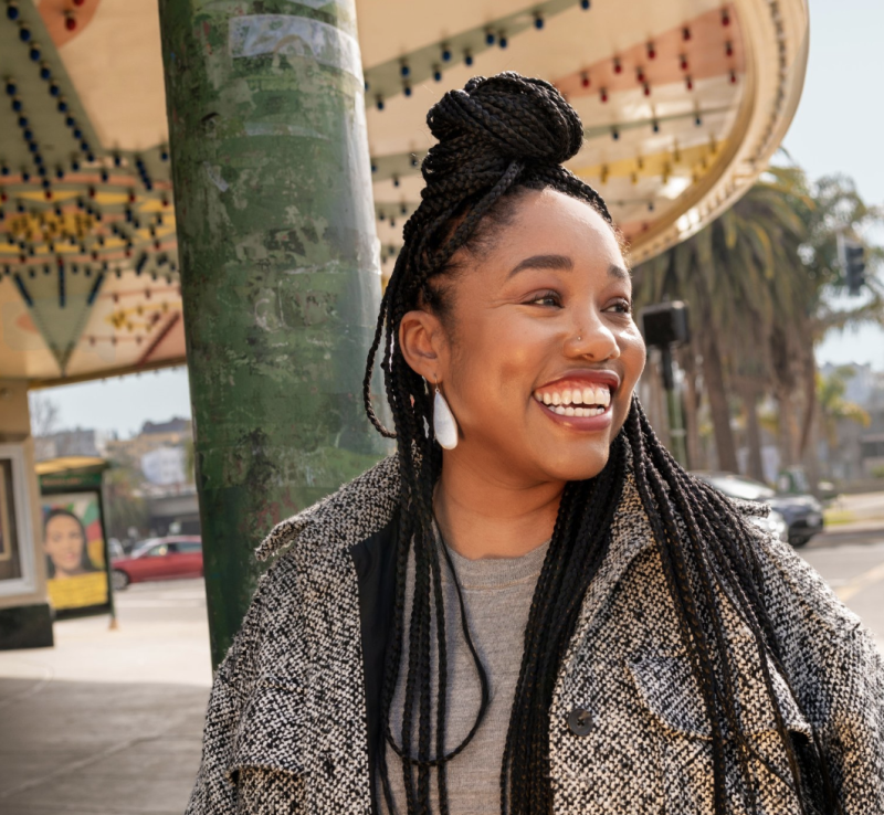 a young Black woman wearing a coat and red lipstick laughs in a portrait