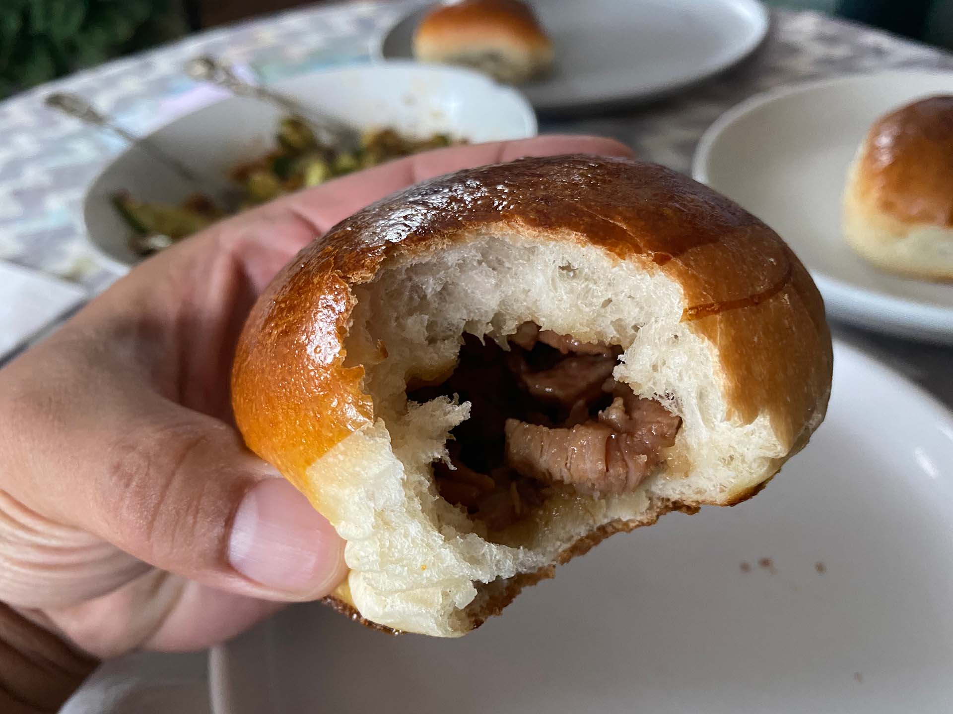A Chinese barbecue pork bun with a big bite taken out of it so that the meaty filling inside is visible.