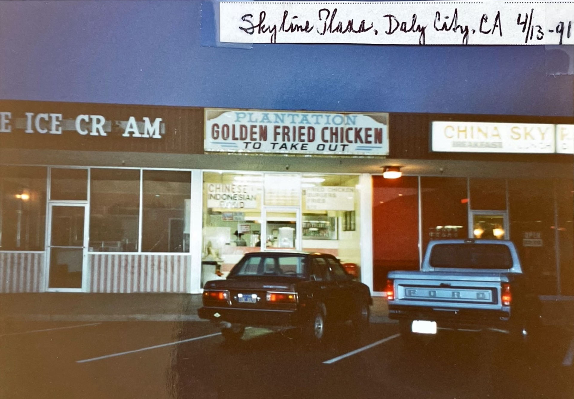 Photograph dated April 13, 1991 shows the facade of a strip mall restaurant at dusk. The sign reads, "Plantation Golden Fried Chicken" in red letters.