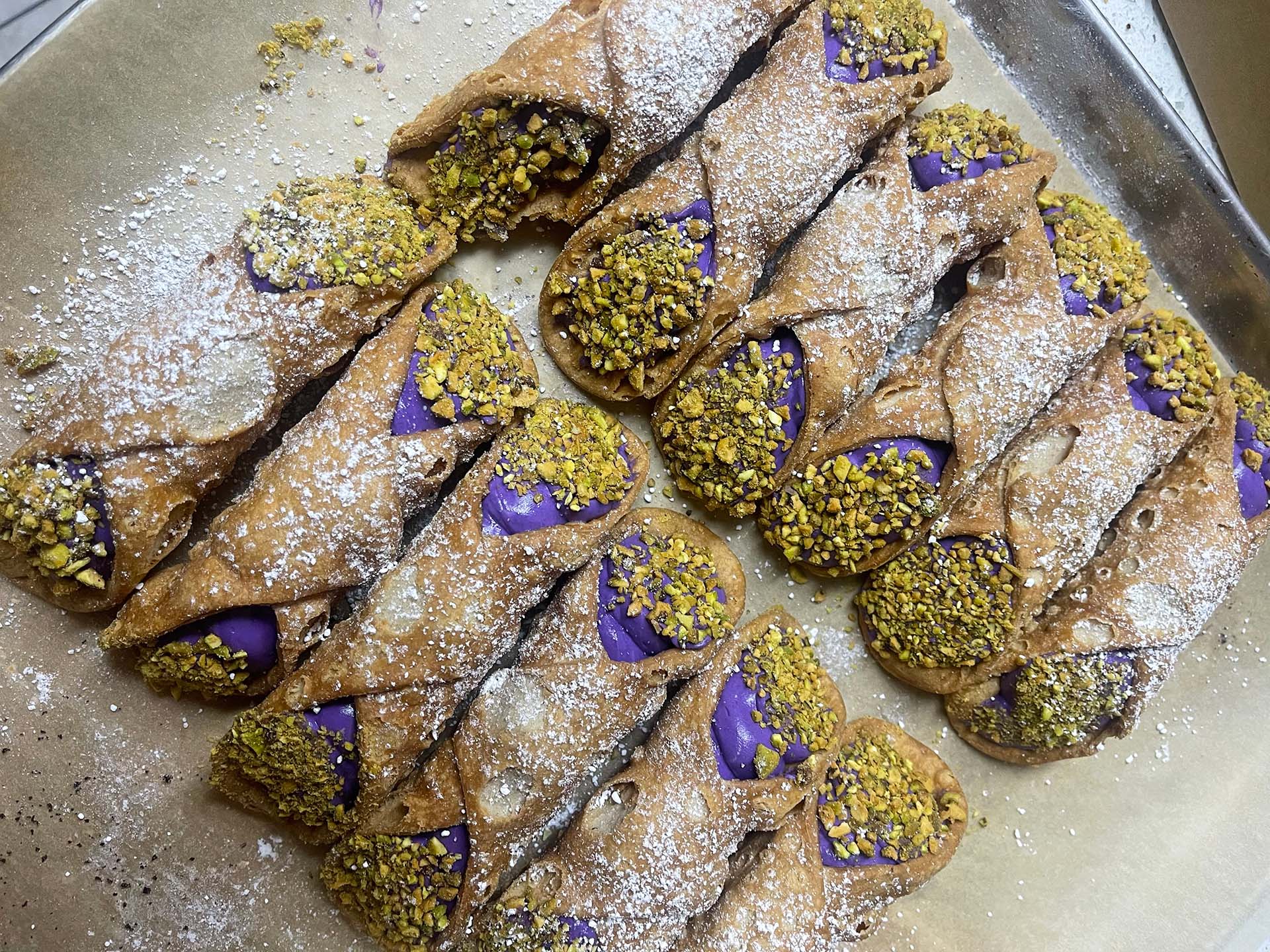 A tray of cannoli stuffed with ube cream and sprinkled with crushed pistachios. 