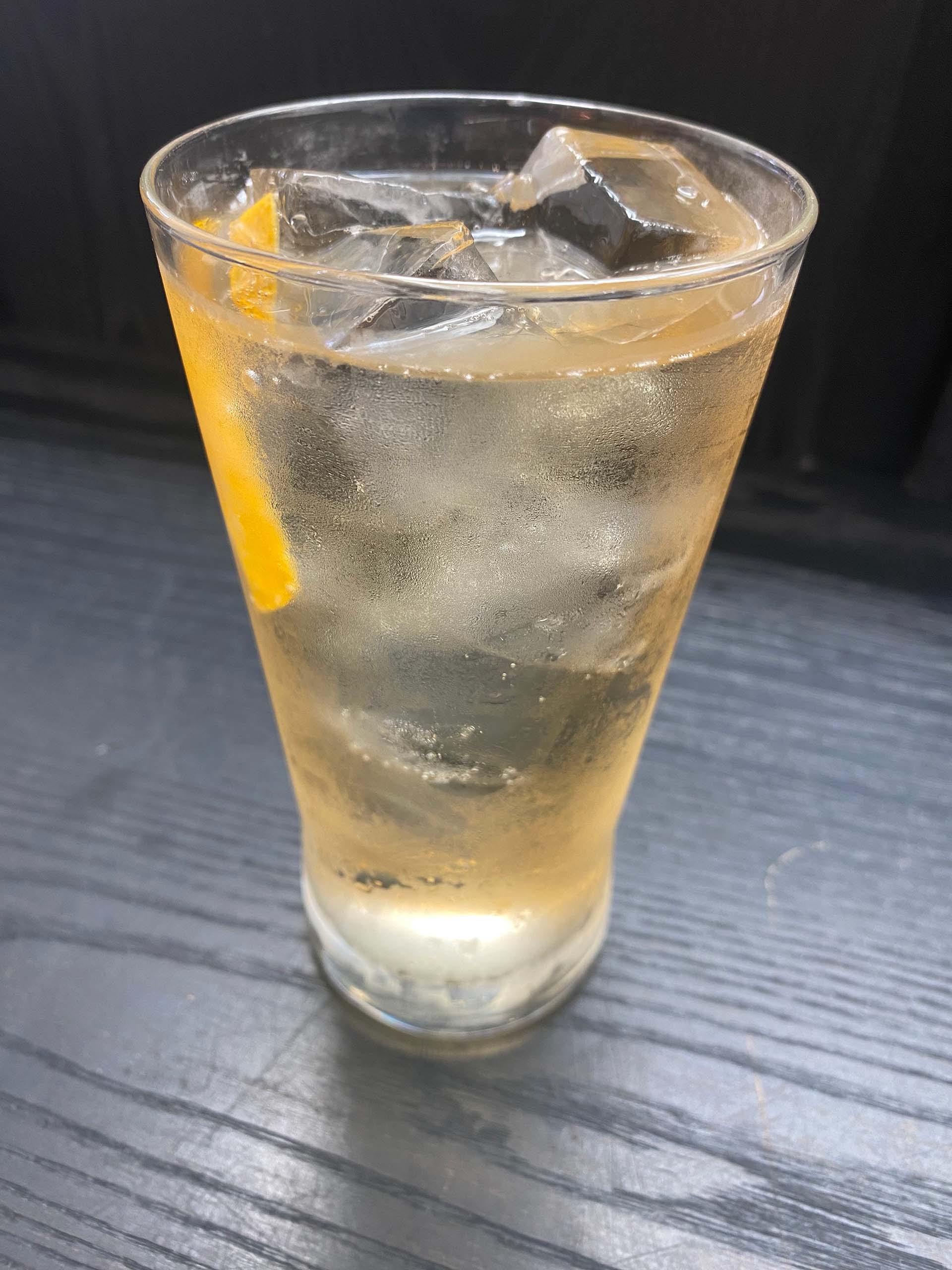 A whisky highball in a tall glass, garnished with a slice of lemon peel.