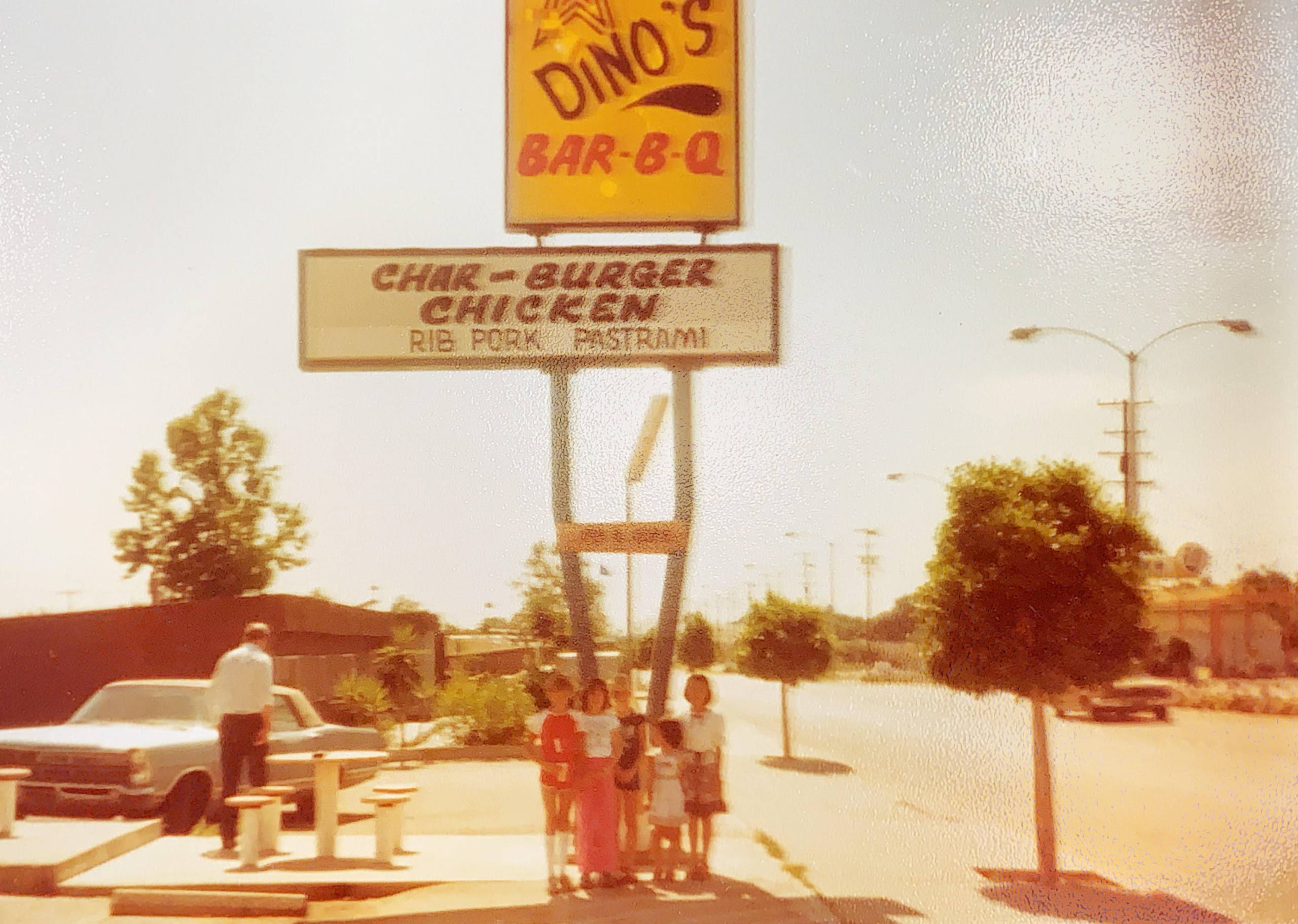 Blurry photograph of five people standing in front of a Dino's Bar-B-Q sign.