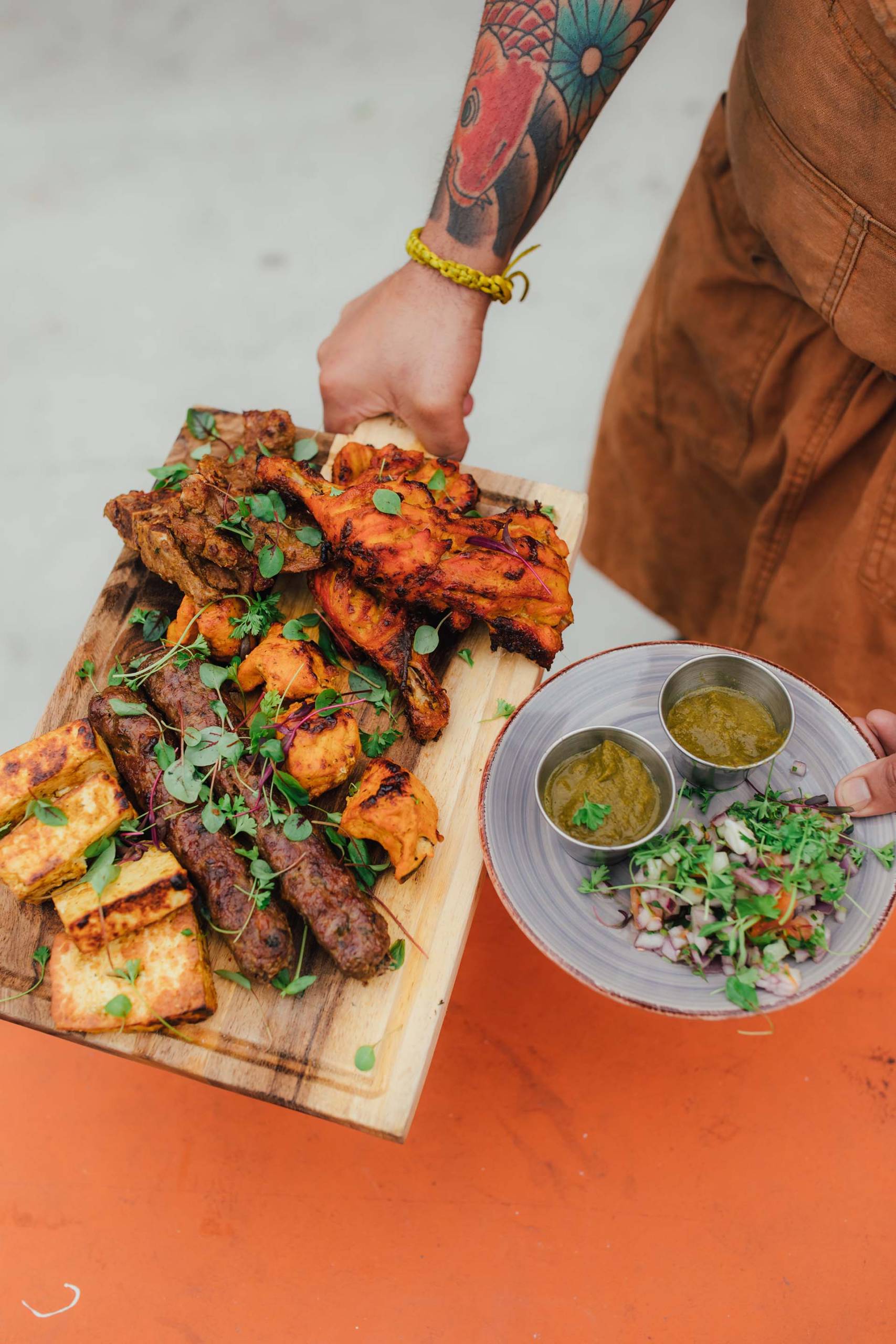 Indian kebabs on a wooden board, with a plate of chutneys on the side.