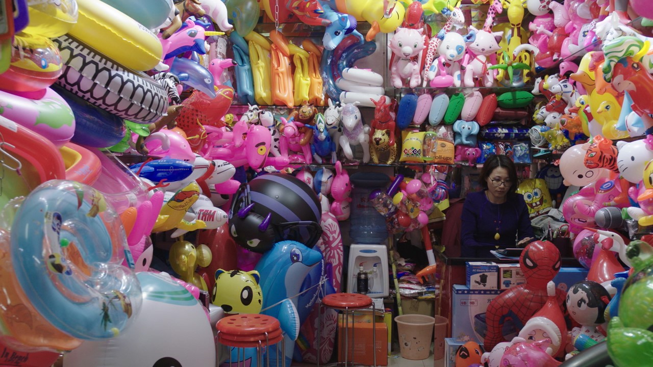 A woman sits in a booth of colorful inflatable plastic toys.