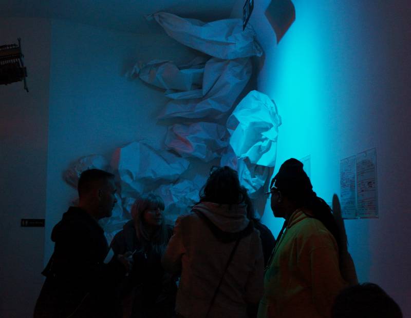 Four figures huddle around a large sound sculpture. They are bathed in blue light.