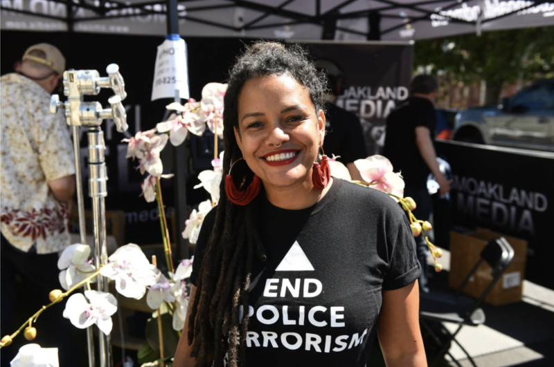 a Black woman with a shirt that reads "end police terrorism" smiles at the camera