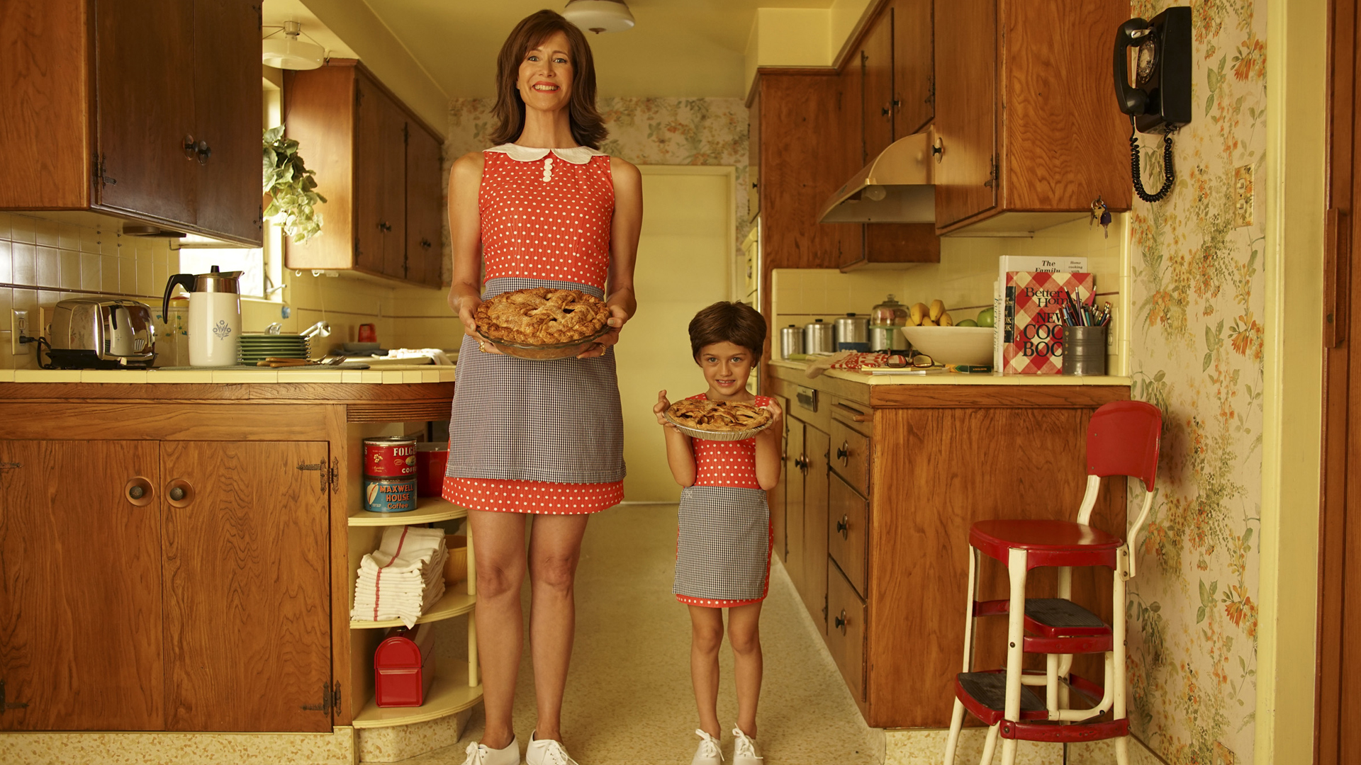 Woman and young girl in matching red dresses hold pies and smile in 70s kitchen