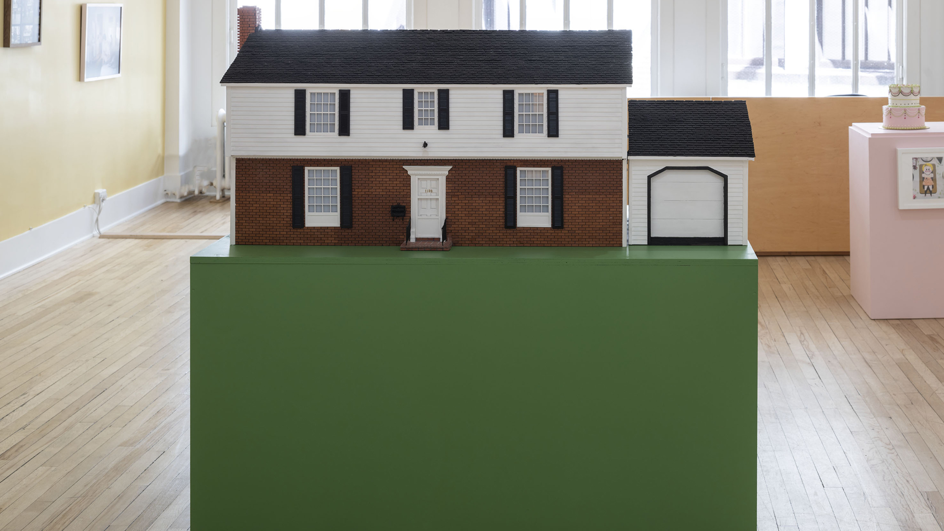 Two-story colonial house with garage as a scale model on a green pedestal