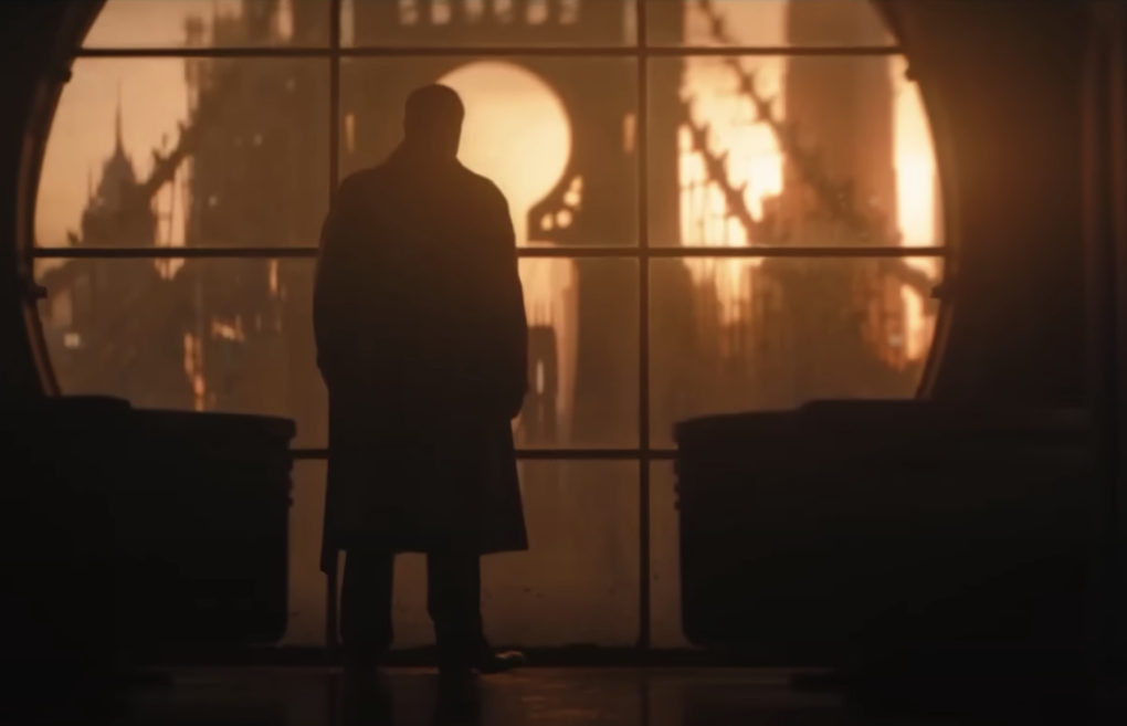 The silhouette of a man wearing an overcoat standing in large windows at dusk, a dramatic bridge in the background.